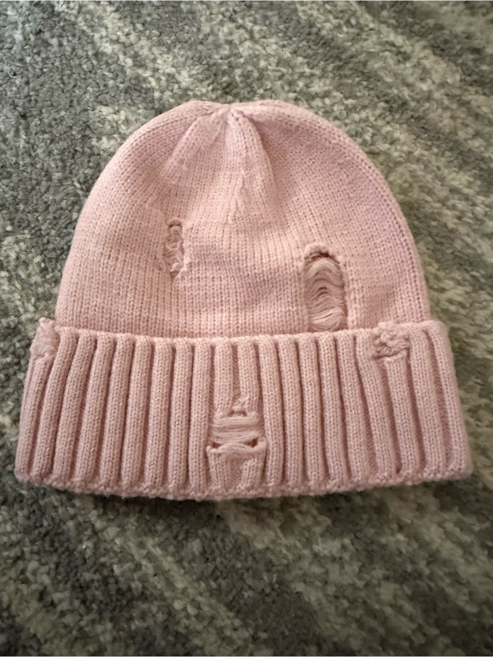 pink, distressed-style knitted beanie (featuring decorative scuffs and "holes”